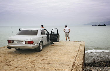 Two men stand net to their Mercedes Benz car by the Black Sea shore in Poti's harbour.