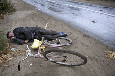 A drunk man lies on the roadside after falling off his bicycle.