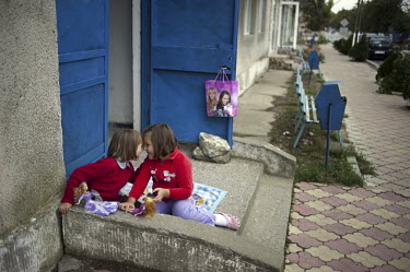 Two girls playing with Barbie dolls at the entrance to an apartment block.