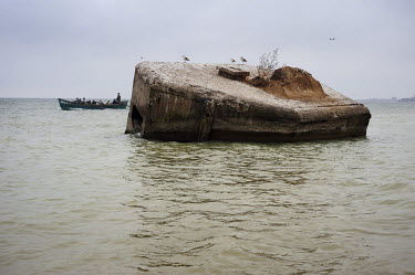 A boat full of fishermen rows past a WWII concrete pillbox half submerged in the waters of the Black Sea.