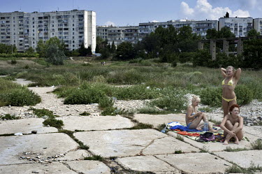 Three young women sunbathe at the edge of a run down Soviet era housing estate by the Black Sea (out of the picture).