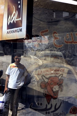 An advert for Laughing Cow cheese is reflected in the glass of a bus stop. Through the glass a young man leans against an advertising sign.