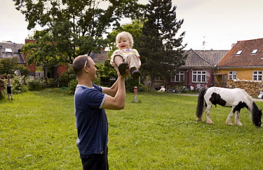 A man holds up a baby in a garden where a horse is grazing in the Christiania neighbourhood of Copenhagen.