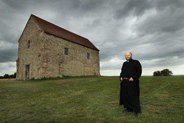 The Reverend Laurence Whitford poses in front of St Peter-on-the-Wall Church of England Chapel in Bradwell-on-Sea, Essex.