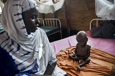A woman sits next to her malnourished baby on a bed in the stabilisation ward at a hospital at Dadaab refugee camp. Since Al Shabaab, an Islamic militia with alleged links to Al Qaida, is controlling...