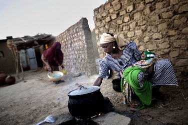 The first wife of Hamidou, Sole, cooks food in the front yard early in the morning. Ouma (14) his second wife stands in the background. In Niger, three out of every four women are married before the a...