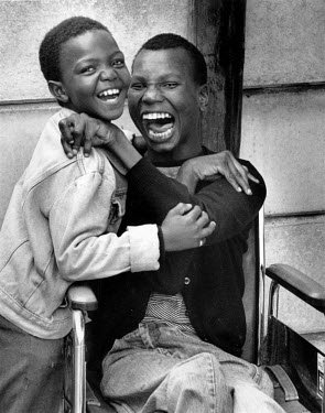 Two pupils in a school of disabled children laugh as they hold each other.