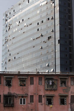 A modern office building being constructed behind an old crumbling residential area.