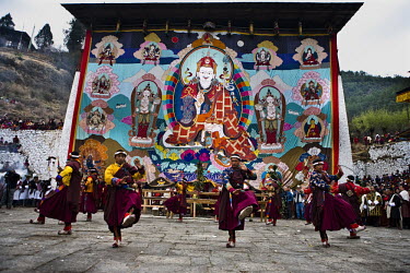 Traditional Bhutanese dancers dance in front of an ancient and giant thangka, a silk painting with embroidery, that is unveiled during a festival in Paro Dzong in Paro, Bhutan.