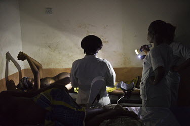 A midwife assists a woman as she goes through labour. Another midwife uses a torch as there is no electricity at the regional hospital in Makeni. A year ago Sierra Leone launched a free healthcare pla...