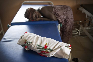 A mother exhausted after giving birth to a still born baby, who is now wrapped in a Christmas cloth at the regional hospital in Makeni. A year ago Sierra Leone launched a free healthcare plan for preg...