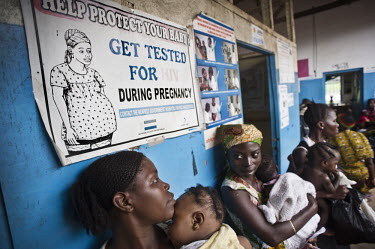 Young mothers and their babies sit beneath a sign encouraging pregnant women to get tested for HIV during their pregnancy at the health centre in the village of Tumbu. A year ago Sierra Leone launched...