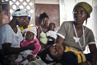 Women sit with their children as they wait for free treatment and vaccinations for their children at a health centre in the village of Waterloo. A year ago Sierra Leone launched a free healthcare plan...