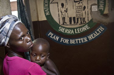 A woman holds her child waiting for free treatment and vaccinations at a health centre in the village of Waterloo. A year ago Sierra Leone launched a free healthcare plan for pregnant women, breast-fe...