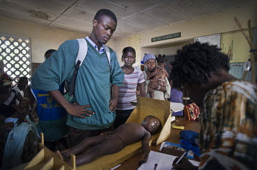 A young man watches as his younger brother is treated at a health centre in the village of Waterloo. A year ago Sierra Leone launched a free healthcare plan for pregnant women, breast-feeding mothers...