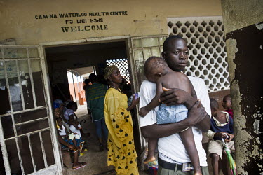 A father carries his son as they leave a health centre in the village of Waterloo. A year ago Sierra Leone launched a free healthcare plan for pregnant women, breast-feeding mothers and children under...