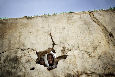 A woman looks through a hole in a security wall that surrounds a Red Cross food storage compound. The rations are usually reserved for women with infants and even then they have to wait several days t...