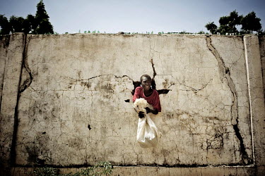 A young boy tries to crawl through a hole in a security wall that surrounds a Red Cross food storage compound. The rations are usually reserved for women with infants and even then they have to wait s...