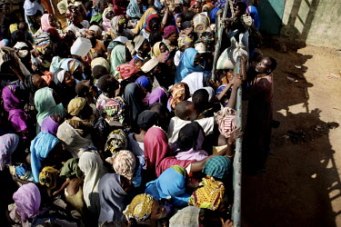 A large crowd of people gather at a security wall that surrounds a Red Cross food storage compound. The rations are usually reserved for women with infants and even then they have to wait several days...