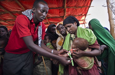 An aid worker takes a mid-upper arm circumference (MUAC) measurement from a child bought to a feeding centre by its mother. The centre is in a camp for internally displaced people (IDPs) near the vill...