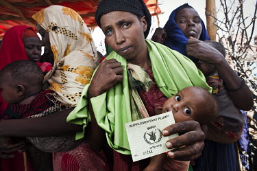 A mother at a feeding centre holds her child and a voucher for Plumpy'nut (Plumpy). Plumpy is a peanut-based highly nutritious supplement given to malnourished children. The centre is in a camp for in...