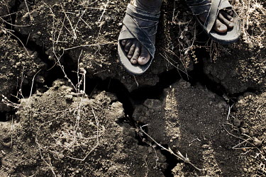 A man stands next to a fissure in the cracked earth, a result of drought.