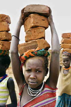 A group of young girls each carrying a load of bricks.