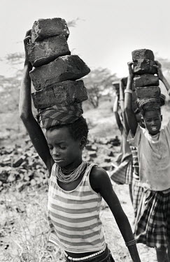 A group of young girls each carrying a load of bricks.