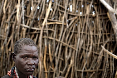 A woman stands within the brushwood walls of her village compound.