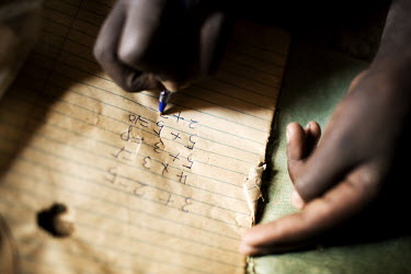 Nanagiro Rose, a young school girl, does her maths homework in the light coming through an opening in her hut.