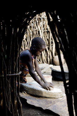 Nanagiro Rose, a young girl, uses a grinding stone to make flour from corn kernals.