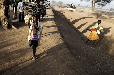 A young girl walks for several hours carrying a load of firewood to sell at a market. She collects the wood from the bush, a task that also takes several hours.