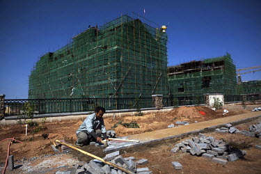 A workers lays paving slabs in front of a construction site in the exclusive Jinxia Hill gated compound where property prices reach 10,000 Yuan per metre. Although most of the complexes are already so...
