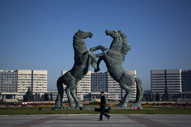 A man walks in front of a giant statue of a pair of rearing horses that stands in front of the government headquarters in Linyinlu Square in the Kangbashi district Ordos. The Kangbashi District of Ord...