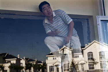 Exclusive villas are reflected in a window behind which a decorator is at work. The Kangbashi District of Ordos, a district planned, five years ago, for 1 million inhabitants, still lies almost dorman...