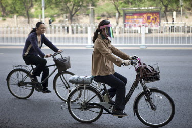 A woman, her face protected behind a sunvisor, rides her bicycle along a road in central Beijing.