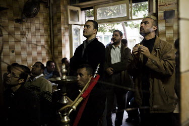 Men eat and smoke sheeshas (hookah, narghile) while they watch television news channels in a tea house just off Tahrir Square during anti-government protests. 25 January 2011 saw the beginning of a na...