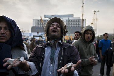 An anti-government protester, with a handful of stones, offers up a prayer during clashes with pro-Mubarak supporters in Tahrir Square. His only protection is a makeshift helmet made of cardboard that...