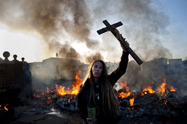 A protester with a crucifix in front of a burning barricade lit to try to prevent the eviction of 86 families from the Dale farm traveller site in Essex.