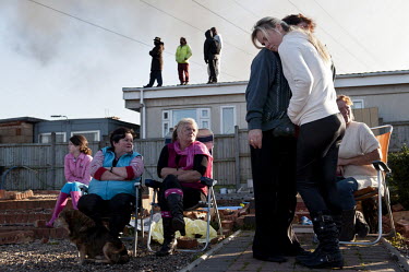 Residents of Dale Farm comfort each other as they watch the eviction of the traveller site in Essex unfold. In the background, protesters occupying a house look on.