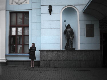 A woman smokes a cigarette as she stands next to a sculpture of a steel worker in the Donetsk train station