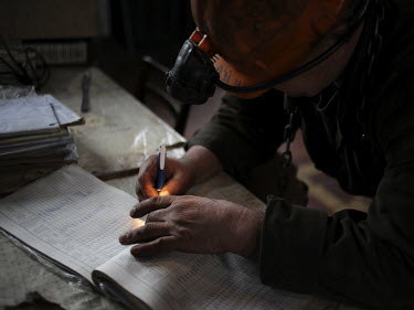 A man uses his helmet lamp to illuminate a form his has to fill out on coming up from the Navagrodovskaya coal mine, West Donetsk.