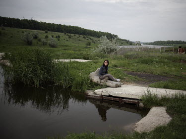 A woman sits by a pond near a countryside datcha.