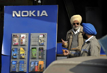 Sikh men with turbans drink tea outside a mobile phone shop.