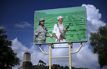 A billboard poster depicting a male and a female soldier from the Eritrean Defence Forces outside a barracks.