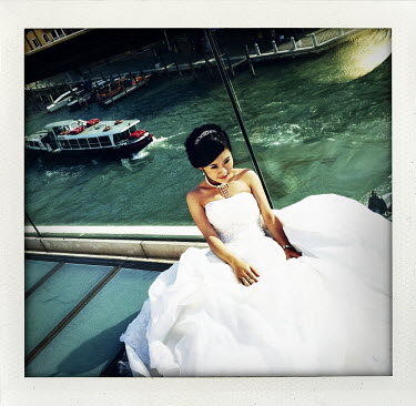 A woman in her bridal gown  sits on a bridge above one of Venice's canals.