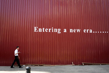 The words 'Entering a new era....' are painted on a temporary wall constructed around the Traders Hotel in central Rangoon (Yangon) which is undergoing renovations with a man walking by in the foregro...