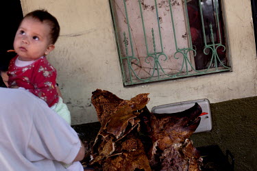 A woman holds a baby while looking at a whole roasted pig during Carnival.