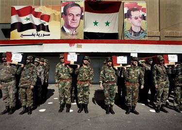Army colleagues carry the coffins of their colleagues from the Syrian Army who have died in fighting around Damascus at their funeral. On the wall behind them images of Hafez al Assad and his son Bash...