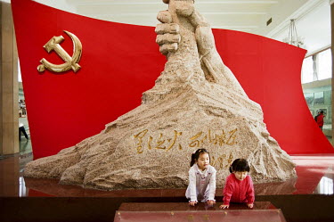 Children visiting the China People's Revolution Military Museum play next to the Monument for the Revolution; a hand holding the barrel of a Kalashnikov gun against the backdrop of the Chinese flag